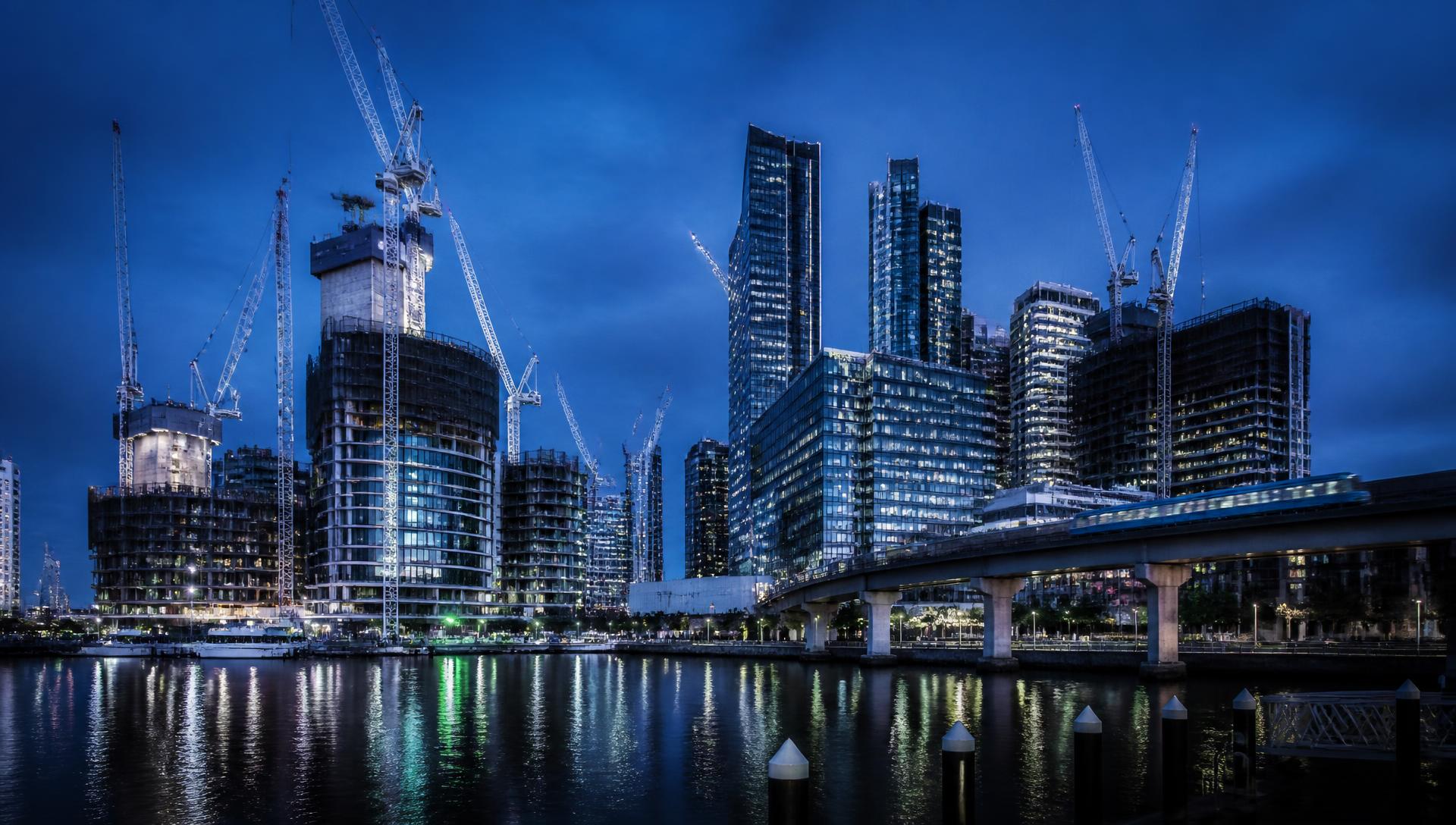 Cranes and high-rise construction over an Australian city waterfront at dusk